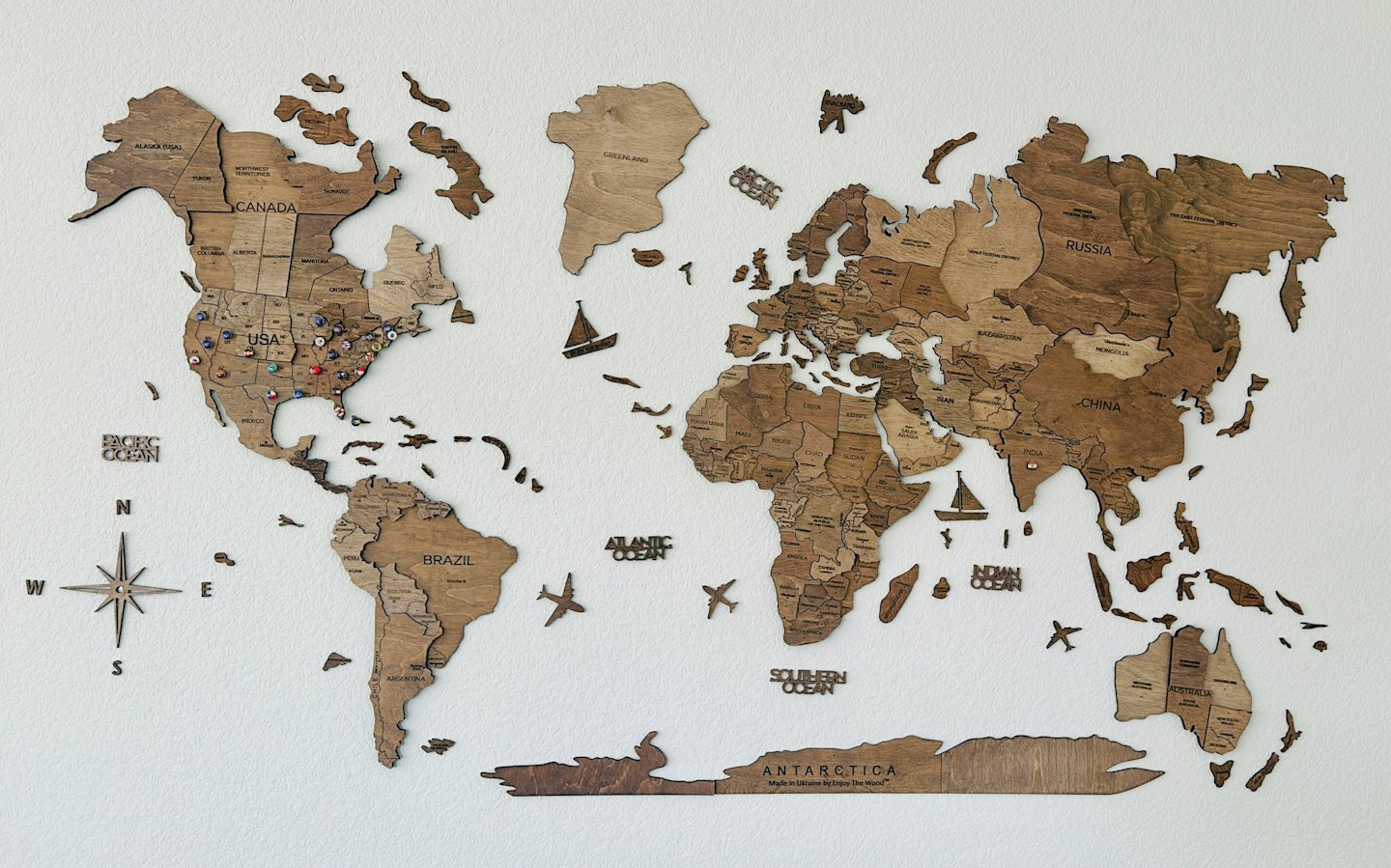 Wooden world map on white wall with pins in North America.